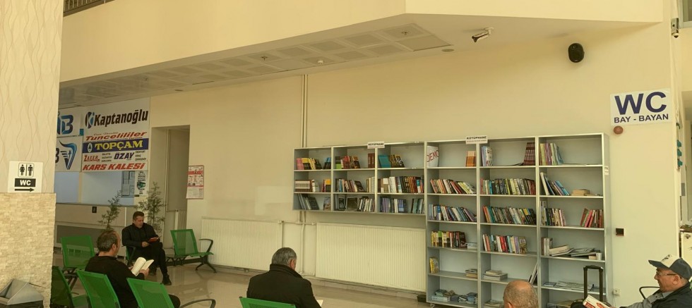 YOLCULAR OTOBÜSLERİNİ KİTAP OKUYARAK BEKLİYOR 